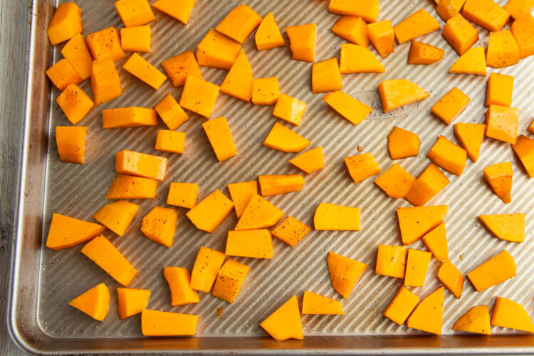 Cubed butternut squash on a silver baking sheet.
