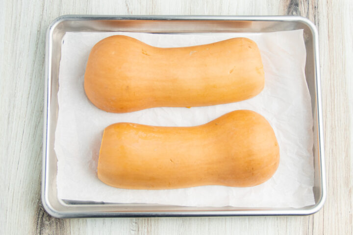 Butternut squash halves on a baking sheet lined with parchment paper.