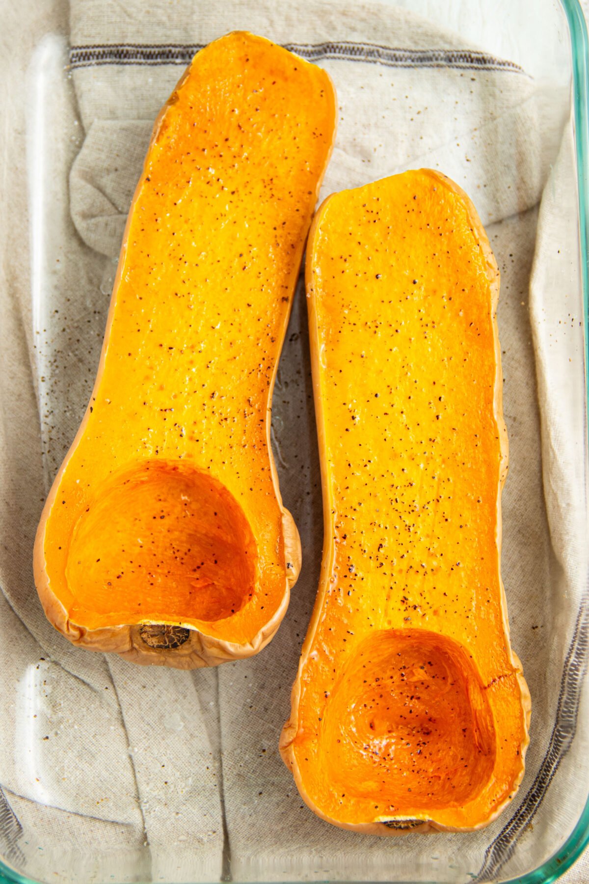 Halved butternut squash in a microwave-safe baking dish.