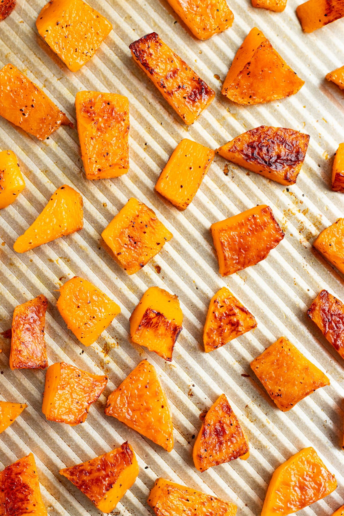 Cubed, oven-roasted butternut squash on a silver baking sheet.