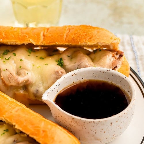Au jus in a small dip bowl next to a French Dip sandwich on a plate.