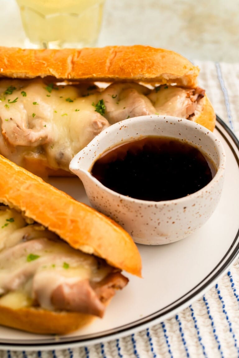 Au jus in a small dip bowl next to a French Dip sandwich on a plate.