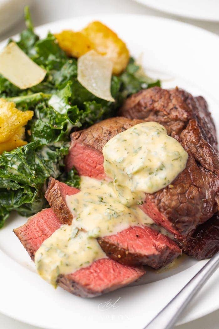 medium rare filet mignon with bearnaise sauce on white plate with kale Caesar salad