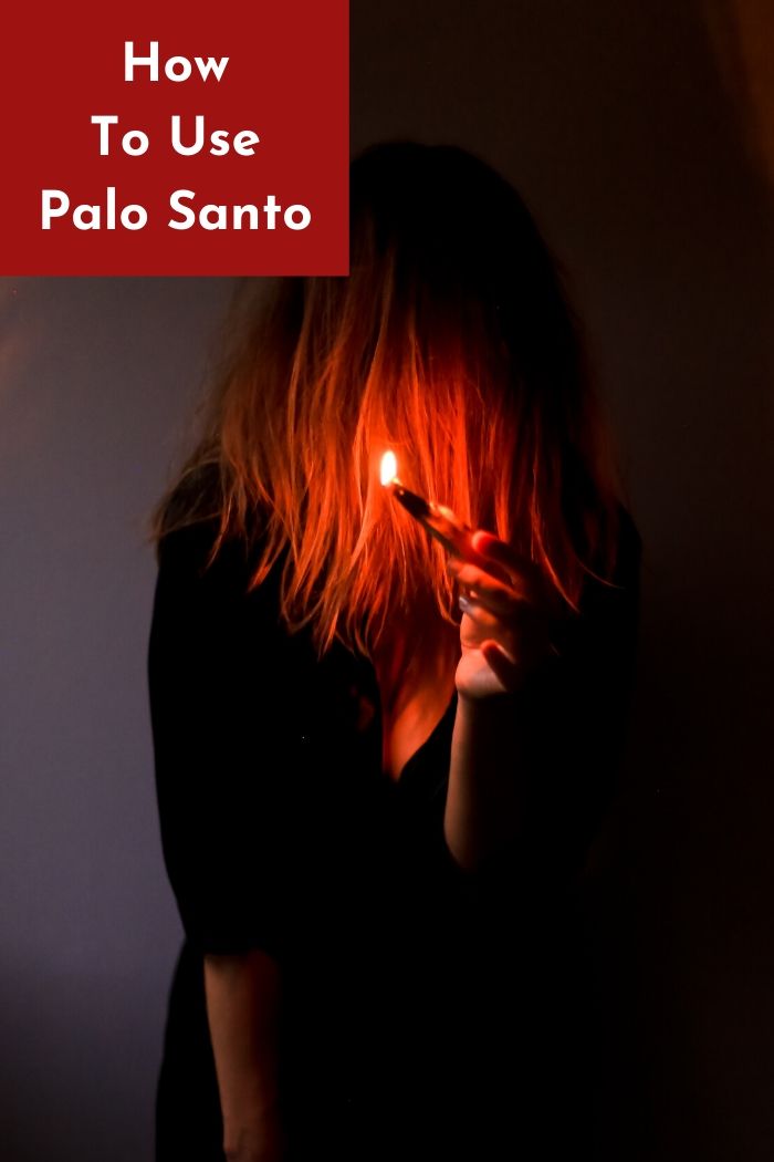 a woman holding a lit palo santo wood stick 