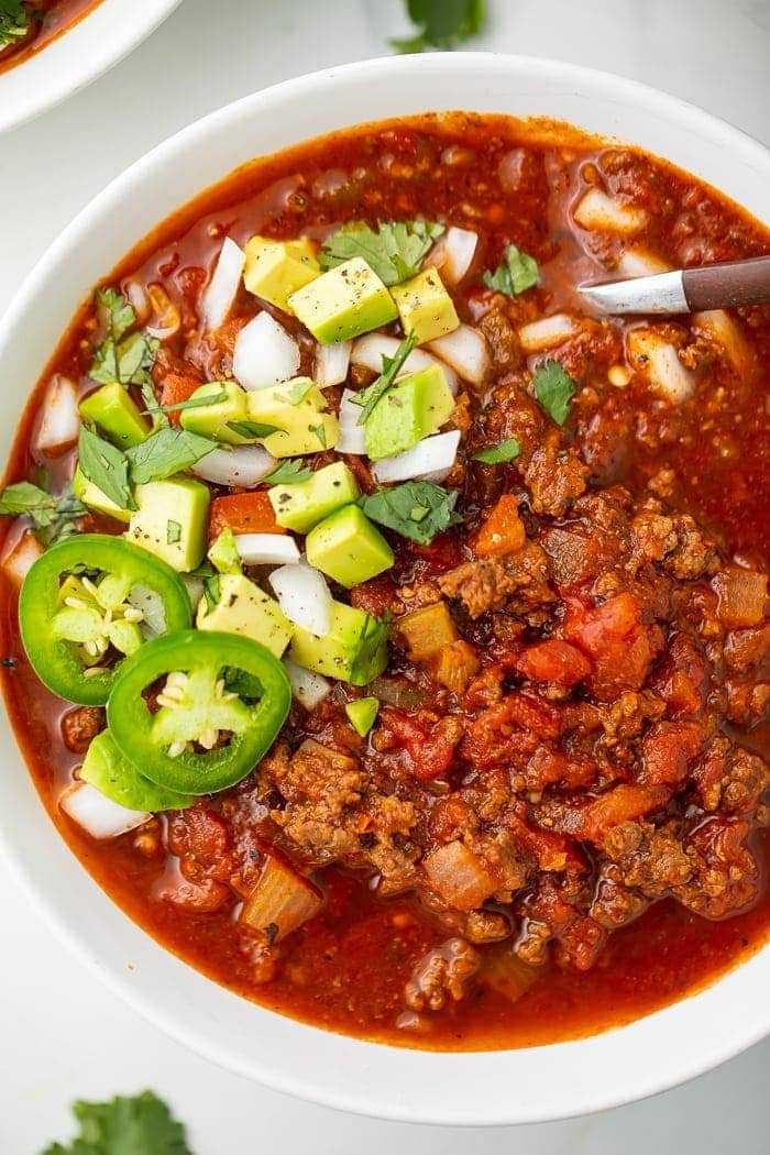 overhead shot of Whole30 chili in white bowl garnished with avocado, jalapenos, onions, and cilantro.