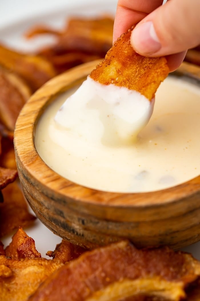 close up image of dipping bacon chips into cheese dip.
