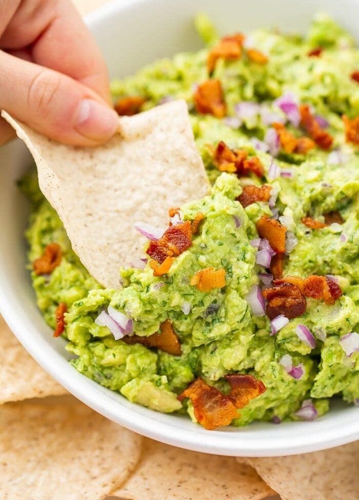 Bowl of bacon guacamole with a tortilla chip being dipped in