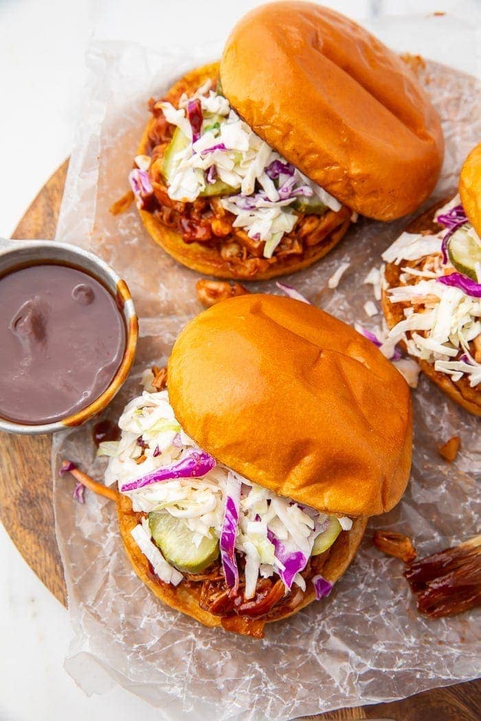 Three vegan BBQ jackfruit sandwiches with a side of barbecue sauce