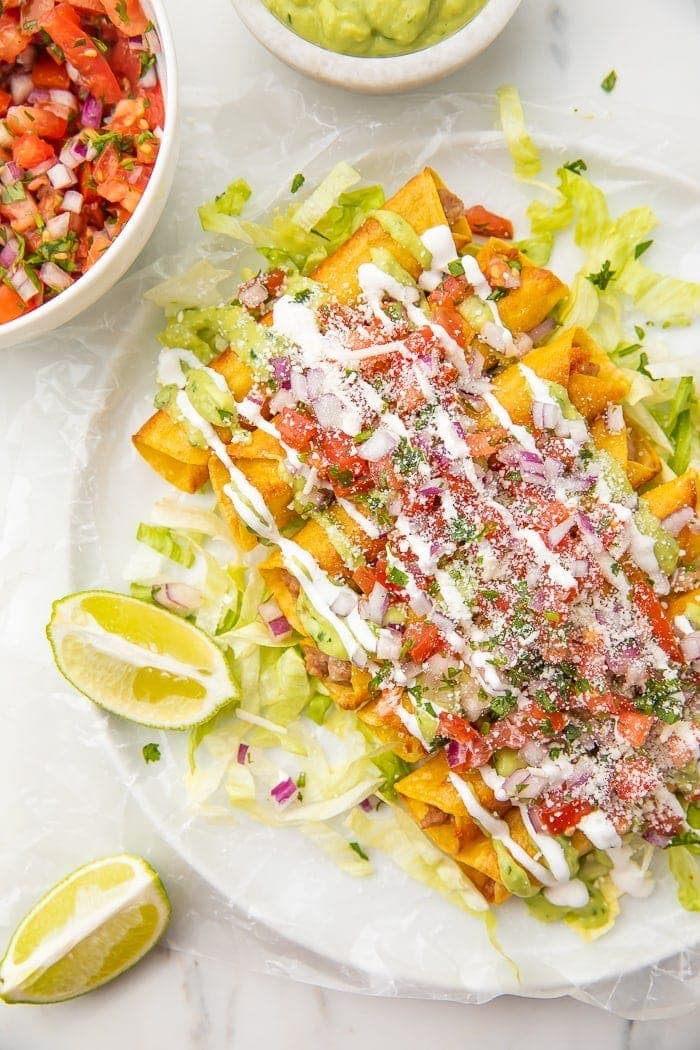 Plate of bean and cheese taquitos with limes and served with pico de gallo and avocado