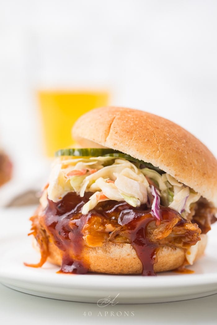 close up image of Instant Pot pulled pork with barbecue sauce, pickles, and coleslaw on bun.