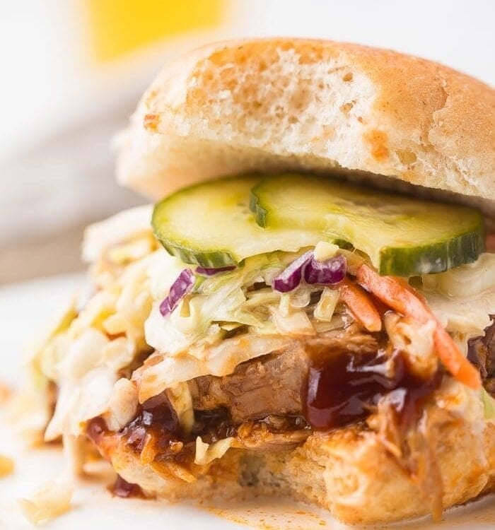 close up image of instant pot pulled pork served on hamburger bun with coleslaw, pickles, and barbecue sauce.