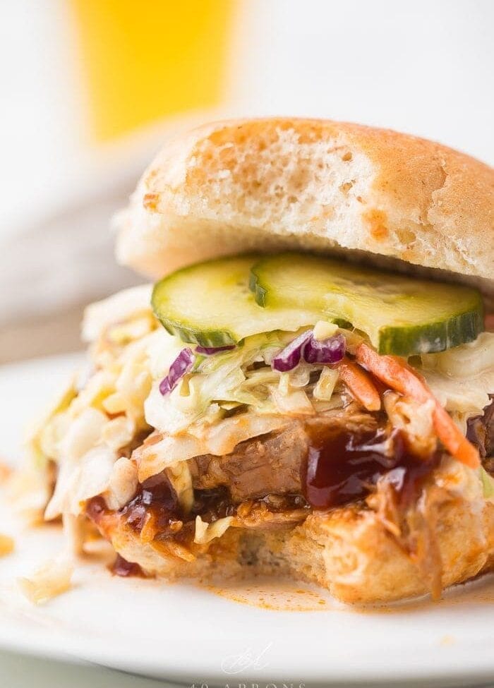 close up image of instant pot pulled pork served on hamburger bun with coleslaw, pickles, and barbecue sauce.