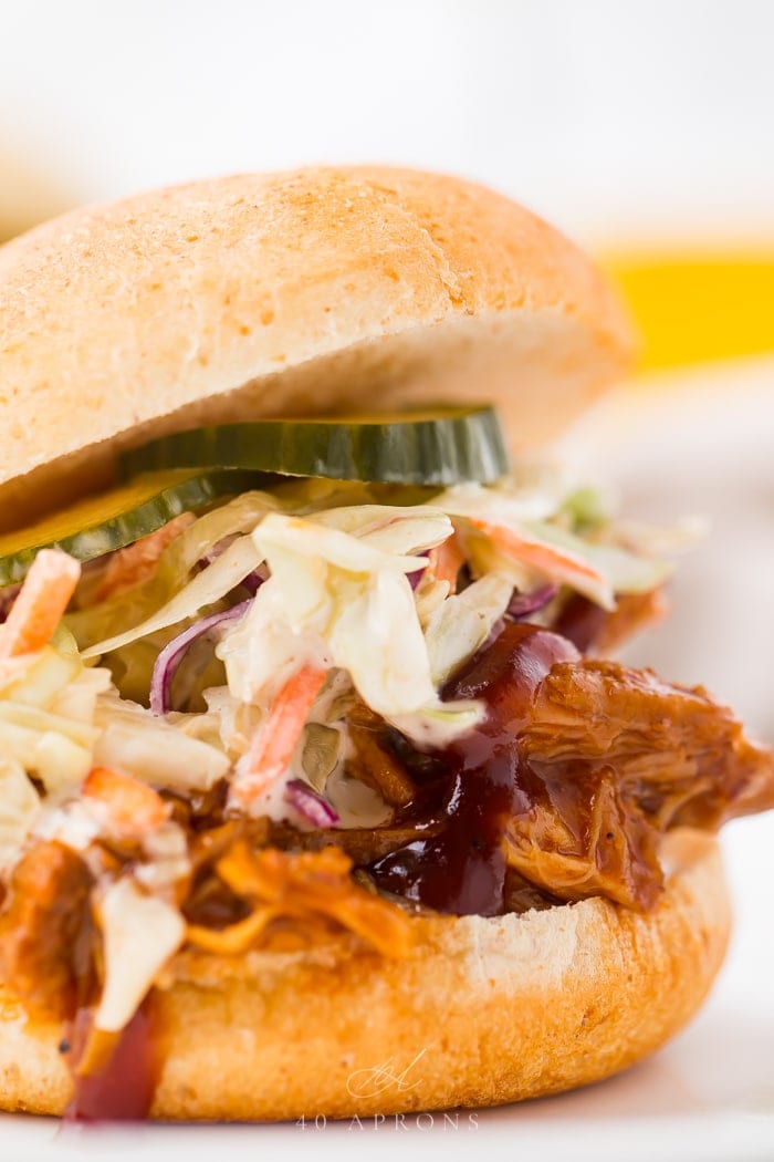 close up image of Instant Pot pulled pork served on hamburger bun with pickles, coleslaw, and barbecue sauce.
