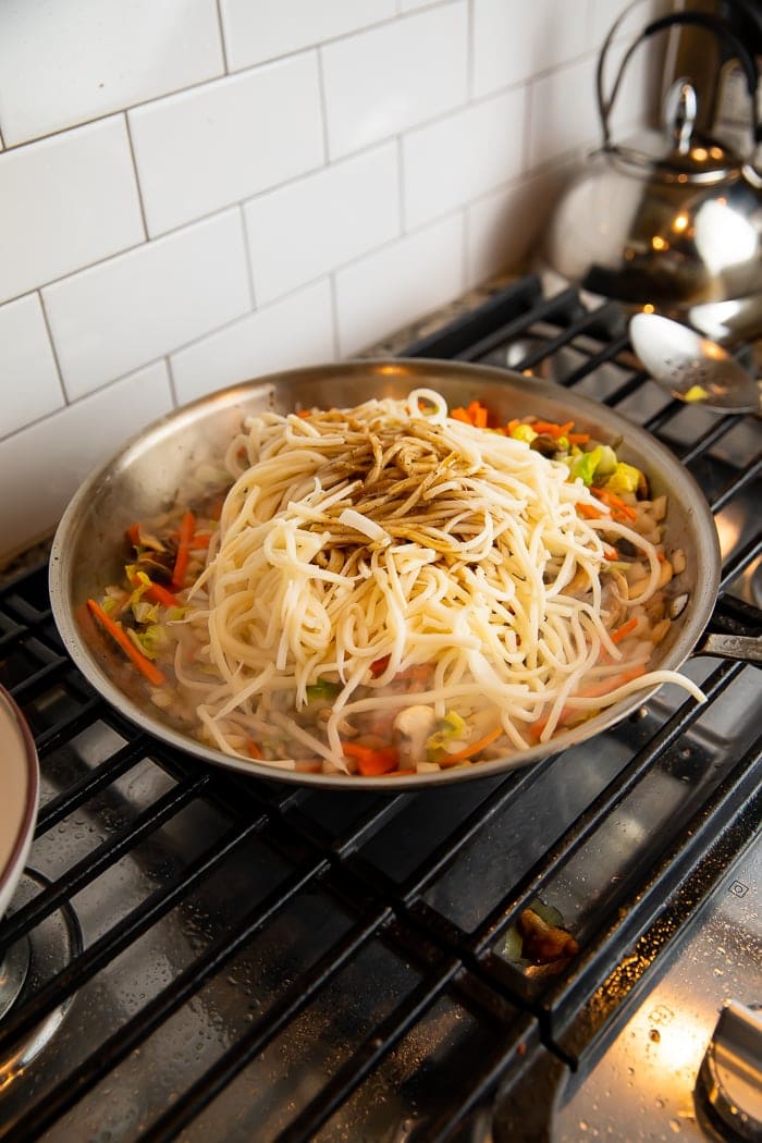 Palmini noodles on top of chicken and veggies in a large wok on a gas stove
