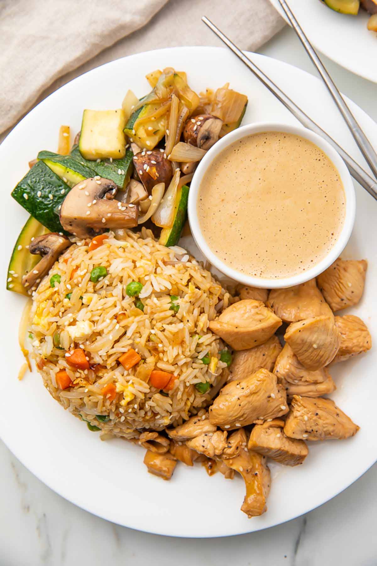 A plate of hibachi chicken and fried rice with hibachi veggies and creamy mustard dipping sauce.