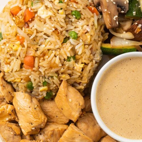 Close-up on a plate of hibachi chicken and fried rice with hibachi veggies and creamy mustard dipping sauce.