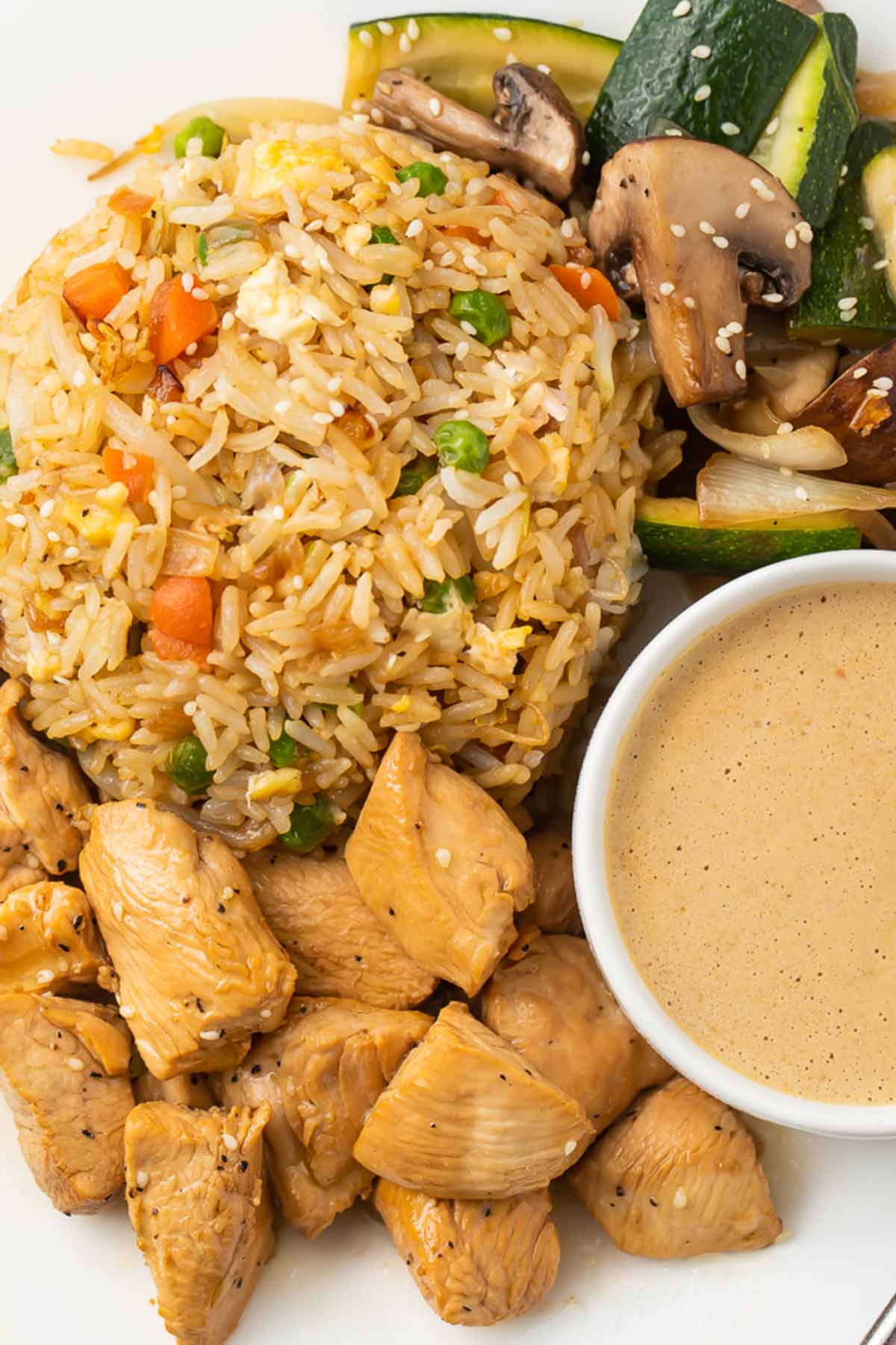 Close-up on a plate of hibachi chicken and fried rice with hibachi veggies and creamy mustard dipping sauce.