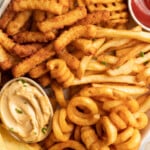 Overhead, closeup photo of various styles of frozen french fries on an oval shaped platter with a ramekin of ketchup