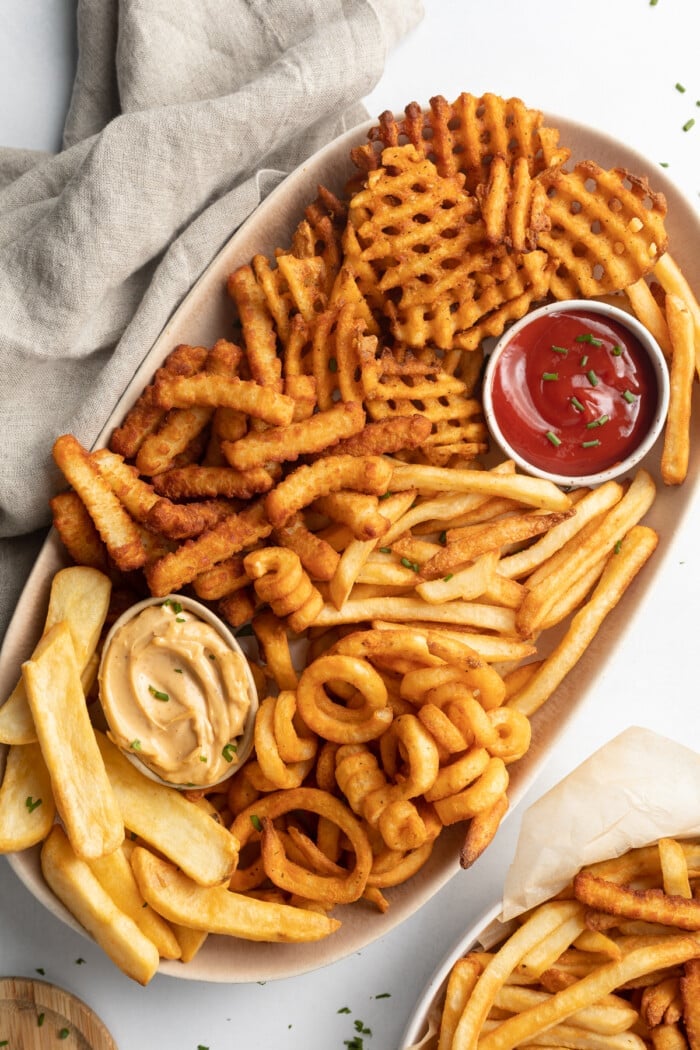 Overhead photo of various styles of frozen french fries on an oval shaped platter with a ramekin of ketchup