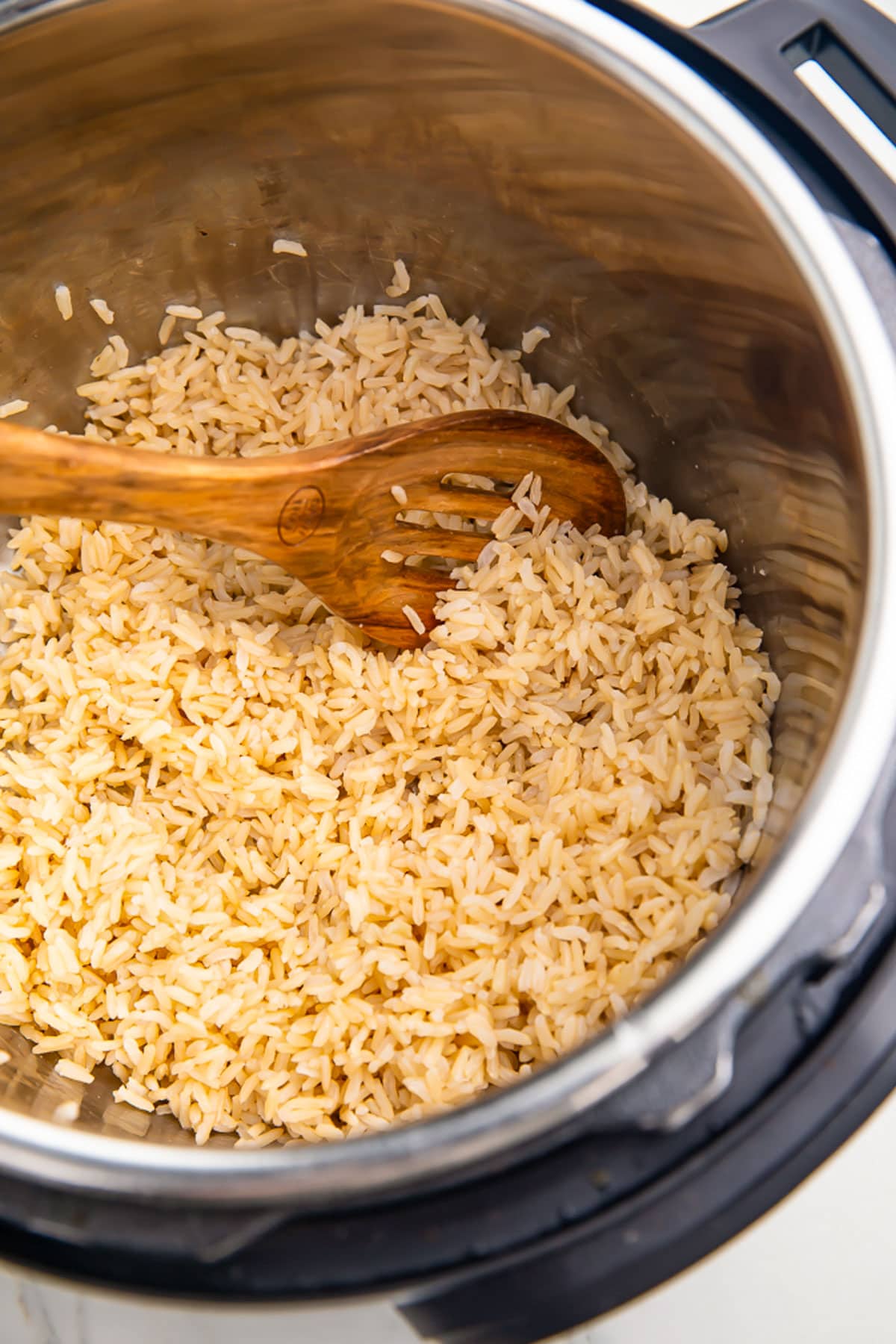 Fully cooked brown rice in an Instant Pot with a brown wooden spoon.