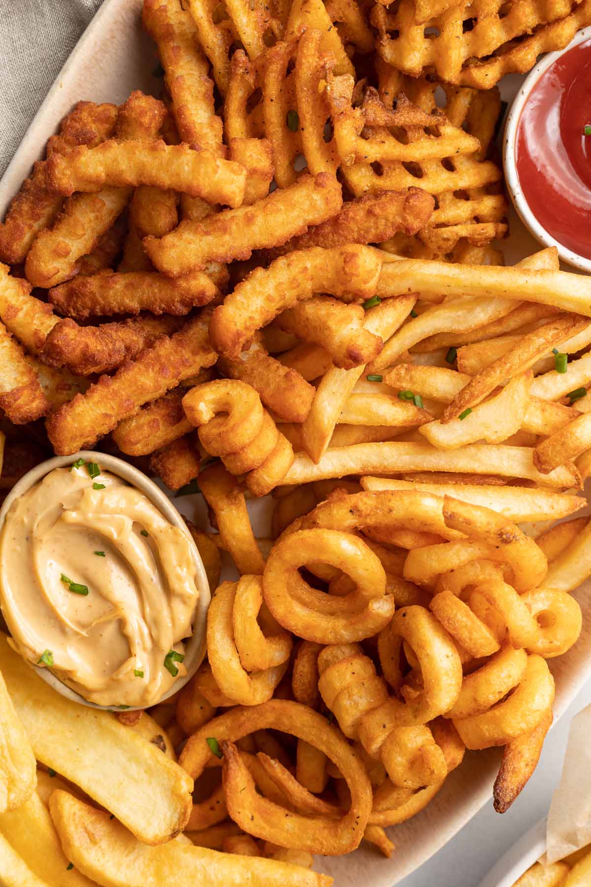 Close-up of different styles of air fryer cooked frozen french fries on a platter.