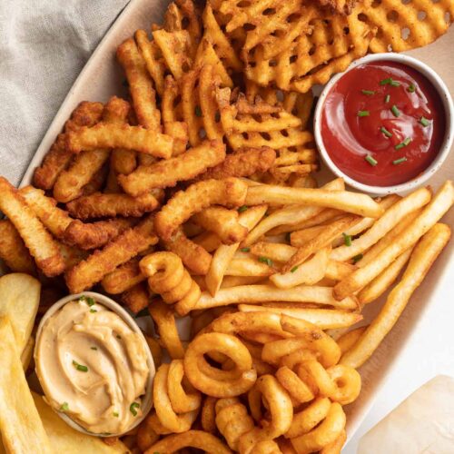 An oval platter of air fryer frozen french fries with 2 ramekins of dipping sauce,