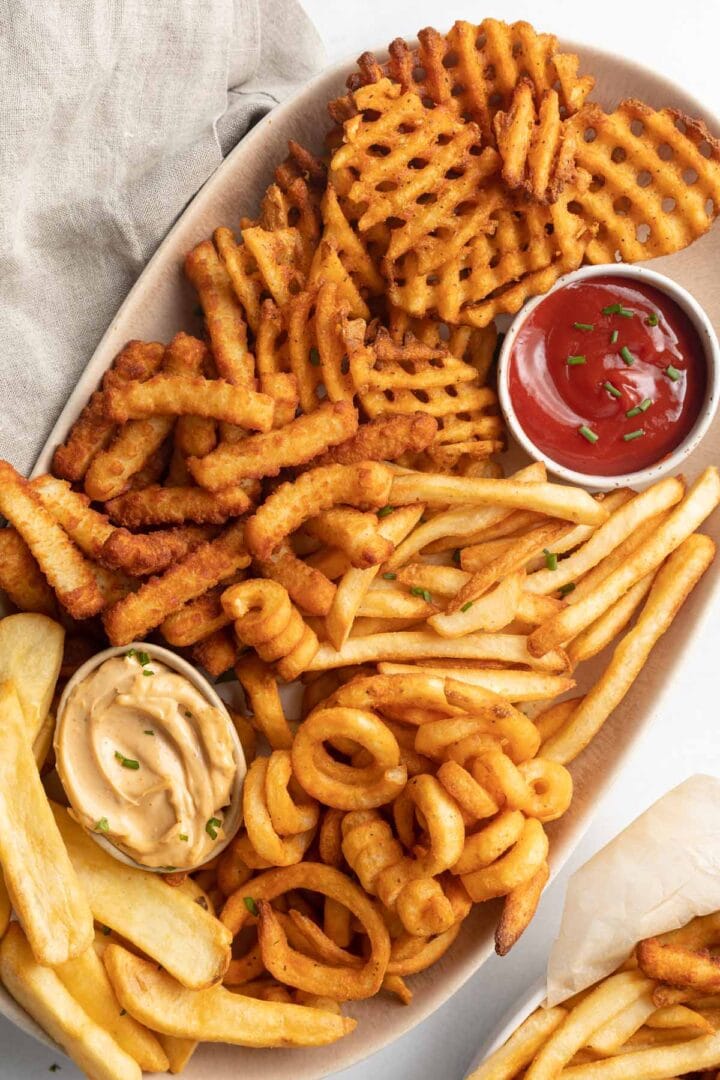 An oval platter of air fryer frozen french fries with 2 ramekins of dipping sauce,