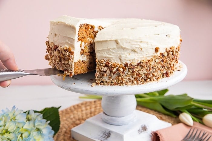 Paleo carrot cake on a cake stand with a piece being lifted out
