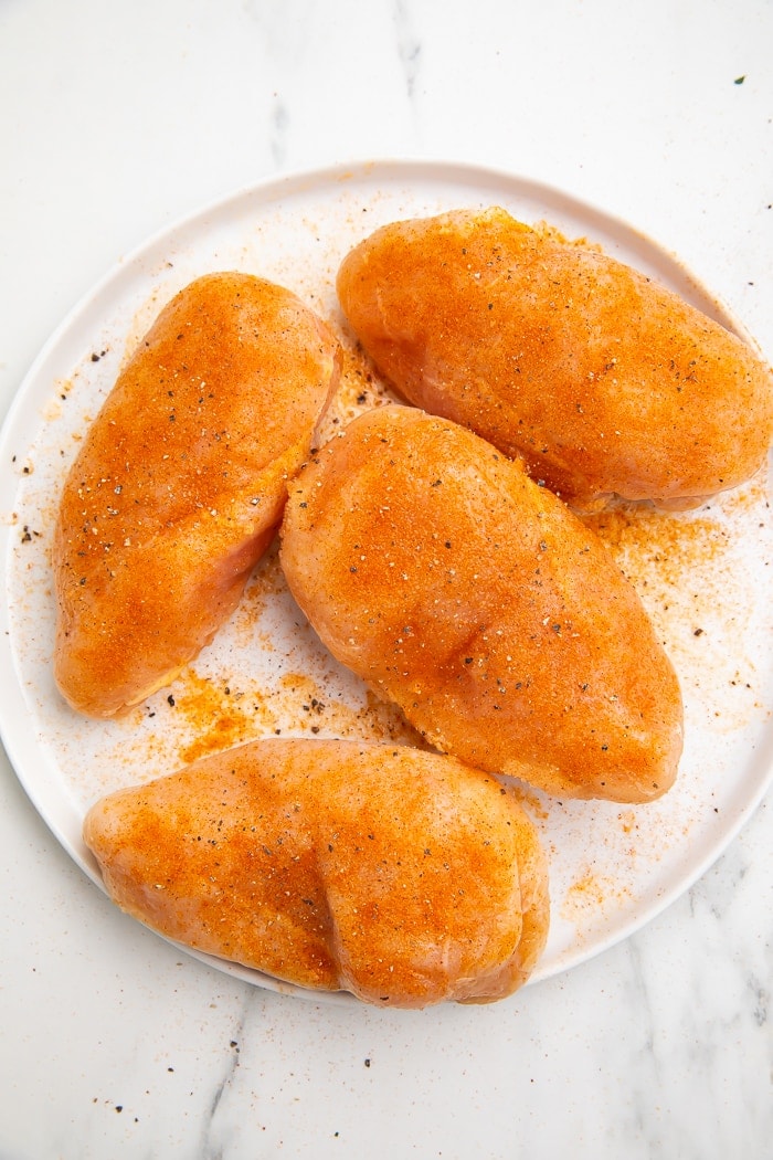 raw frozen chicken breasts on a white plate with seasoning