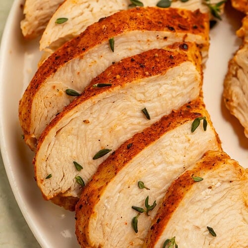 Sliced cooked chicken breast with seasoning on a white plate.