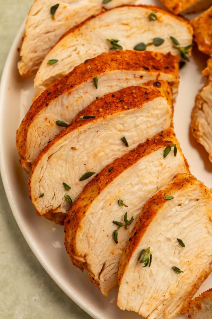 Sliced cooked chicken breast with seasoning on a white plate.