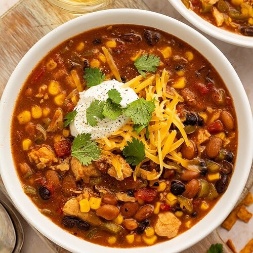 8-can taco soup in white bowl with sour cream, shredded cheese, and cilantro next to glass of white wine
