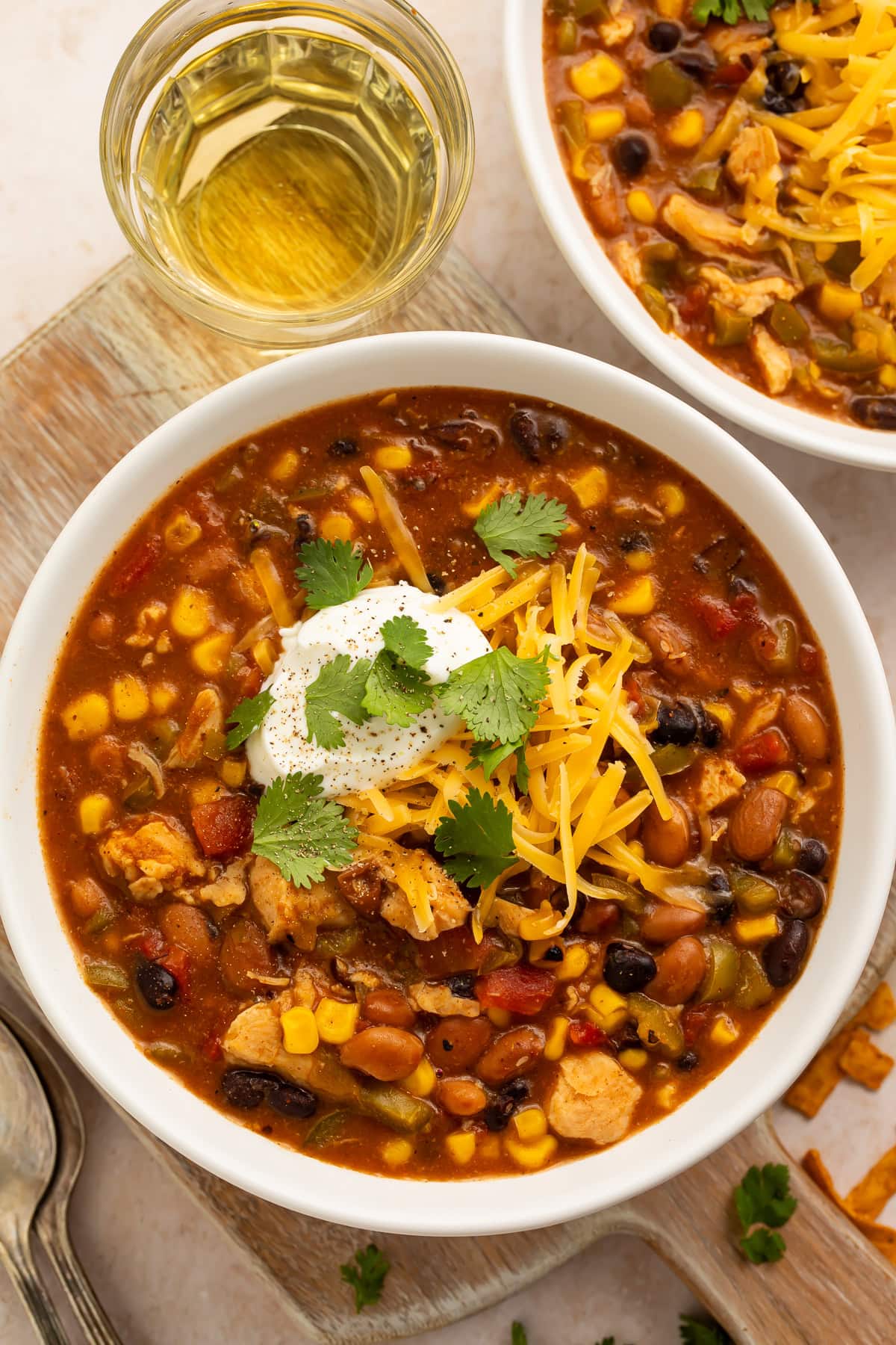 8-can taco soup in white bowl with sour cream, shredded cheese, and cilantro next to glass of white wine