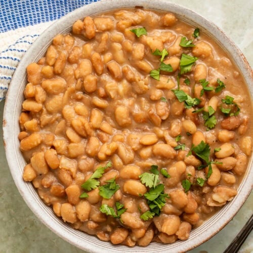 White bowl of cooked pinto beans with chopped cilantro scattered on top.