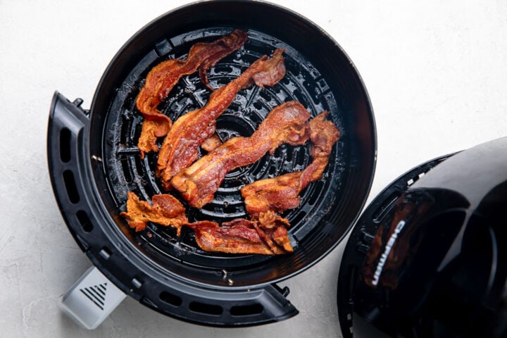 Fully cooked strips of bacon in a round air fryer basket.