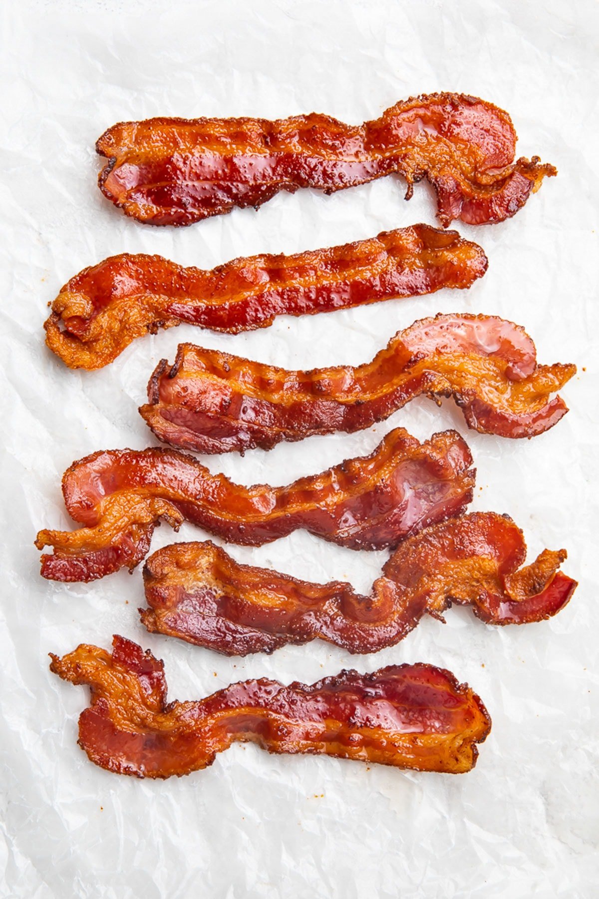 Overhead view of crispy strips of air fryer bacon on a sheet of parchment paper.