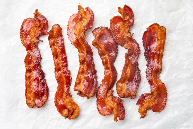 Strips of crispy air fryer bacon on a sheet of parchment paper.