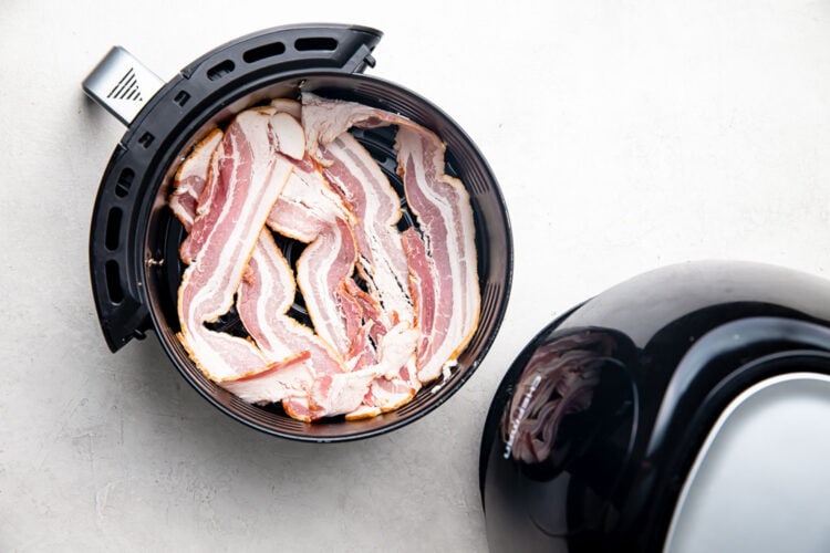 Strips of uncooked bacon in a small Chefman air fryer basket.