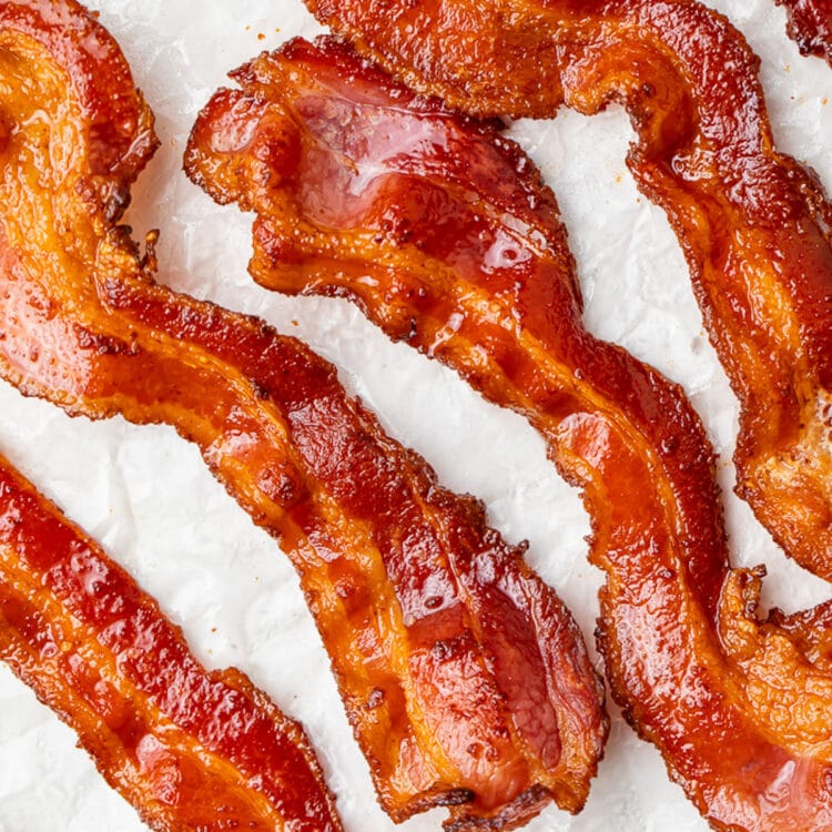 Air fryer bacon strips placed on a sheet of parchment paper, positioned at an angle.