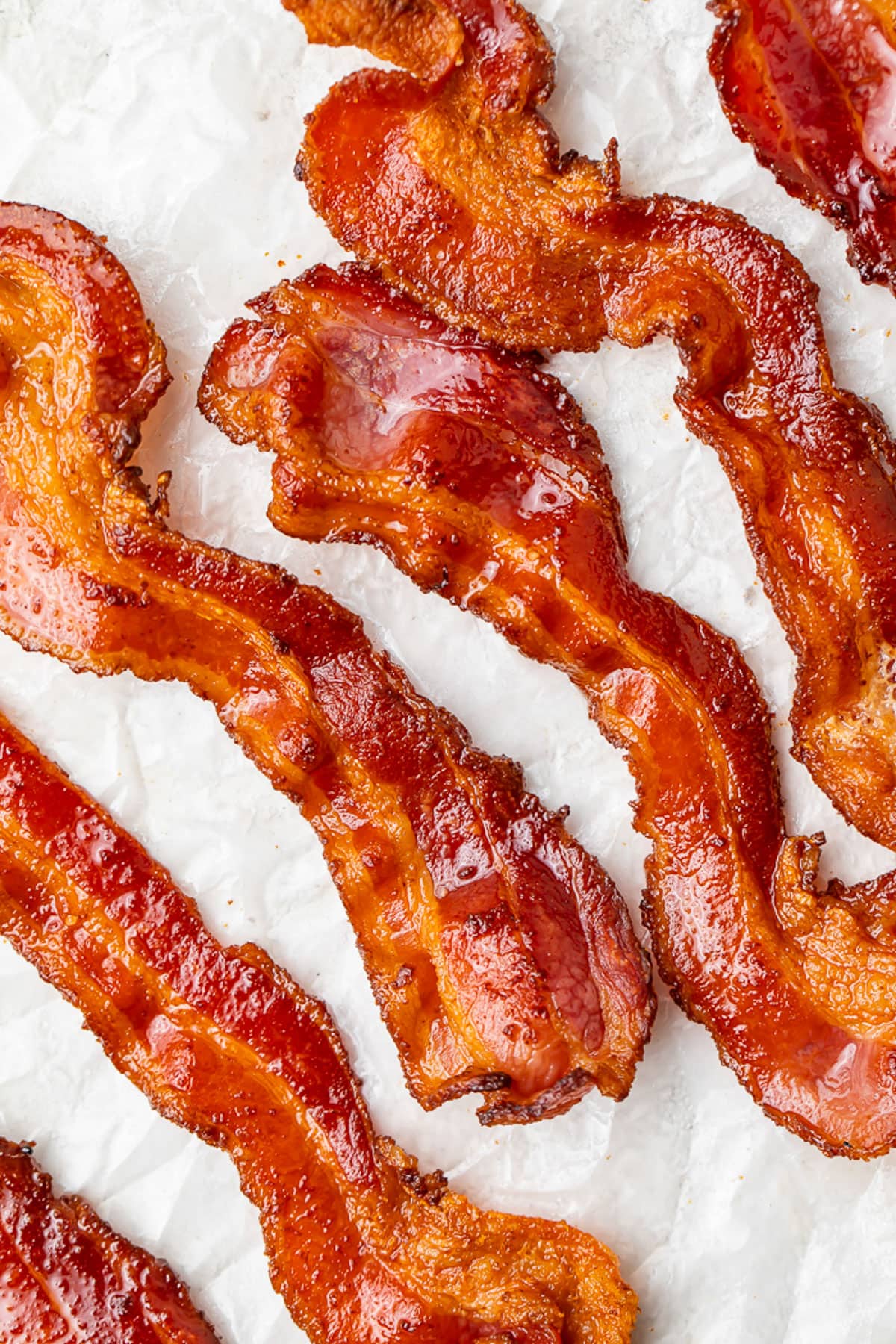 Air fryer bacon strips placed on a sheet of parchment paper, positioned at an angle.
