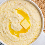 Overhead view of creamy grits in a white bowl, with a pat of melting butter swirled in the center of the bowl.