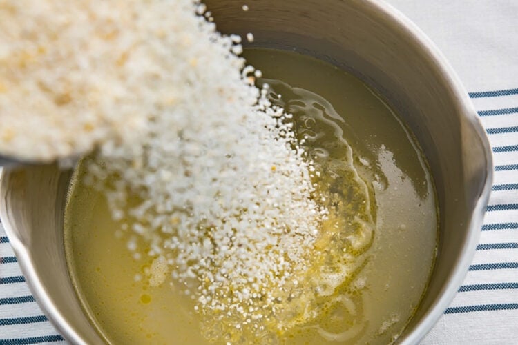 Grits being added to salted water and melted butter in a medium silver saucepan.
