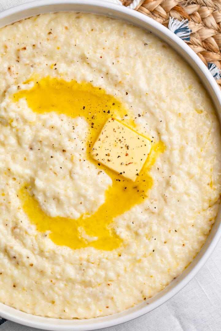 Overhead view of creamy grits in a white bowl, with a pat of melting butter swirled in the center of the bowl.