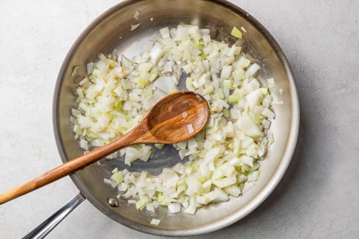 Chopped onions and minced garlic in a large silver skillet with a wooden spoon.
