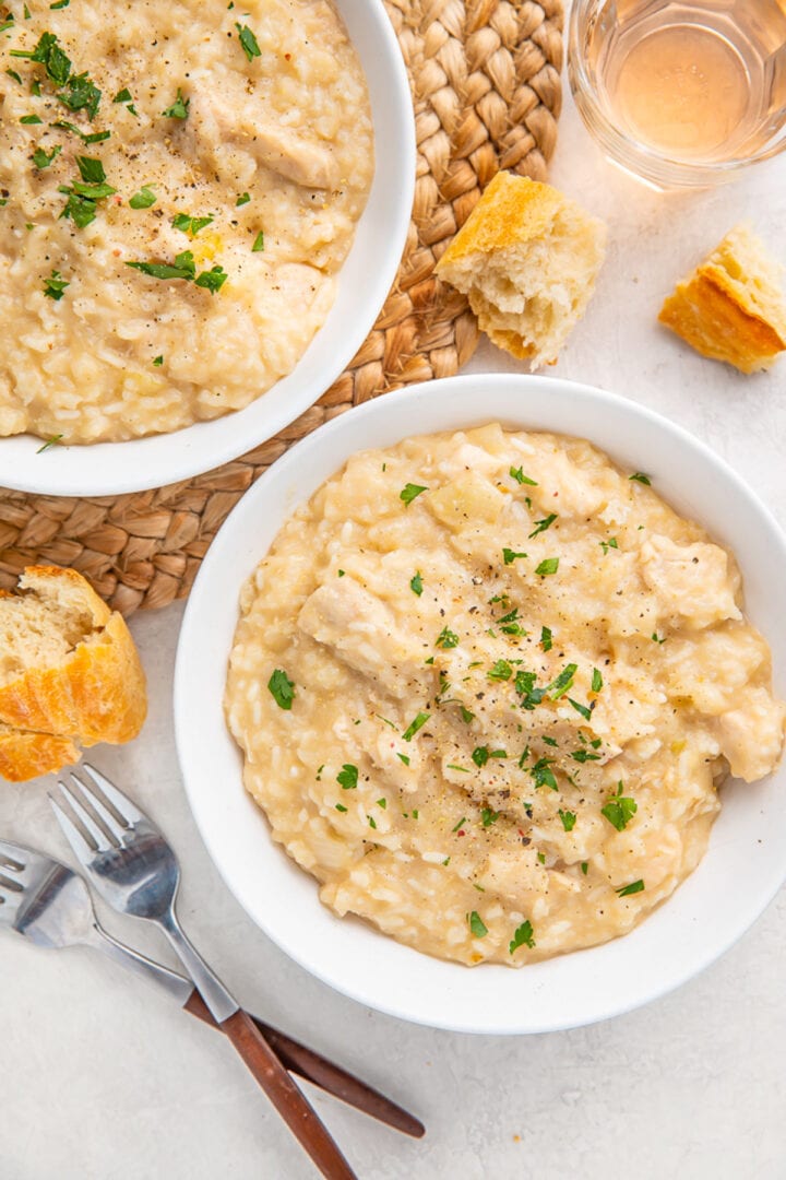 Two bowls of Crockpot chicken and rice on a white table with a wicker placemat underneath.