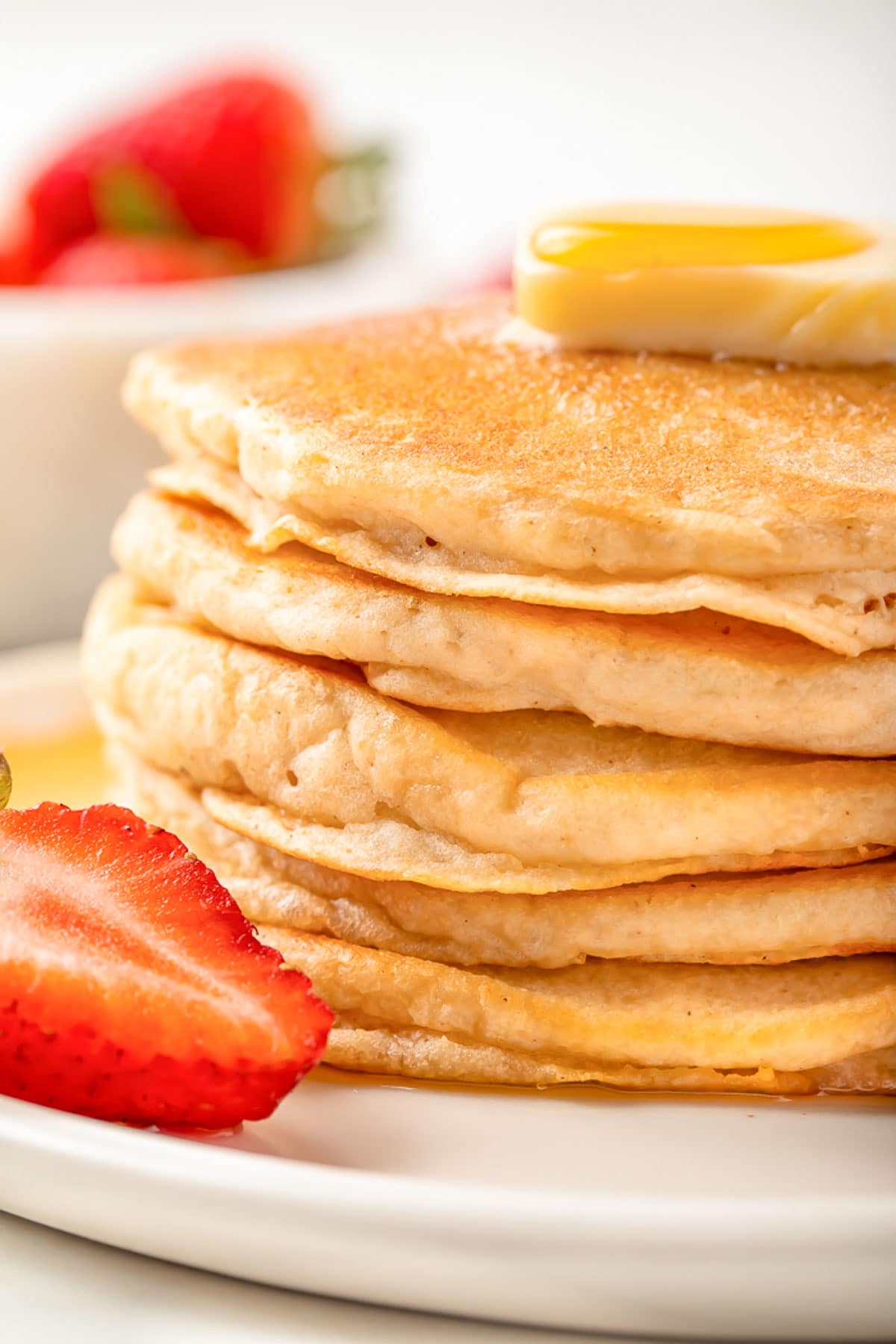 A stack of fluffy, gluten-free pancakes on a white plate with a halved strawberry.