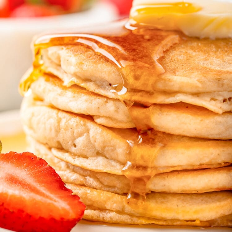 Syrup being poured over a stack of fluffy gluten-free pancakes topped with a pat of butter.