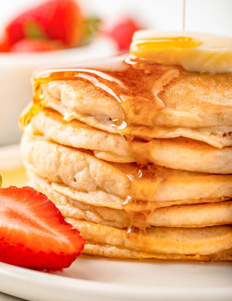 Syrup being poured over a stack of fluffy gluten-free pancakes topped with a pat of butter.