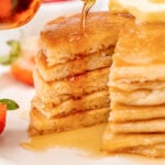 Syrup poured over a stack of gluten-free pancakes after a wedge has been cut out.
