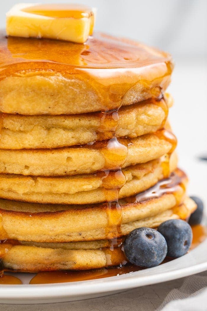 Stack of paleo pancakes with a pat of butter and syrup with blueberries to the side